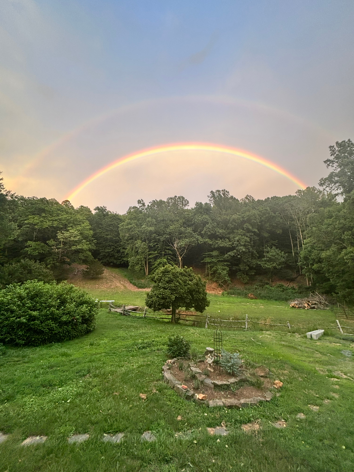 A double rainbow arching over the green fields and forest at Free Holler Farm